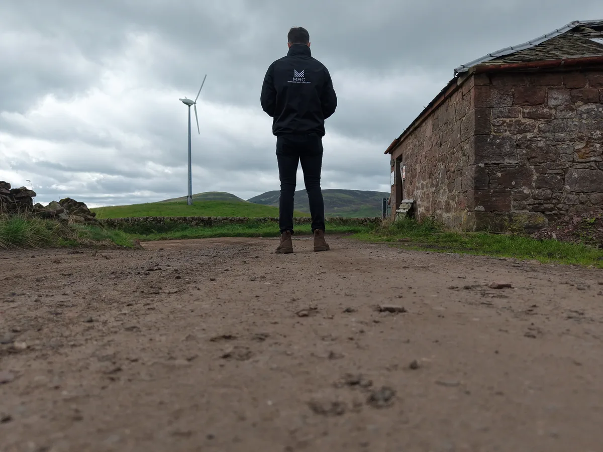 Person overlooking a wind turbine on rural land